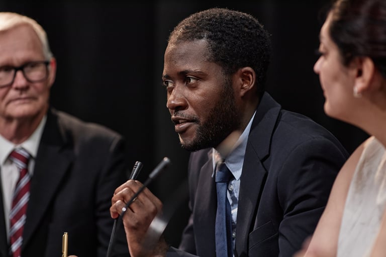 Confident African American politician speaking into microphone giving report on law reforms while sitting with group of other officials during press conference