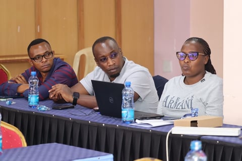 Three men seated at a conference panel table with water bottles and laptops during a professional event