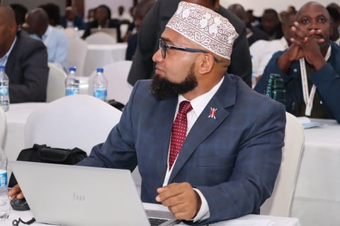 Man with beard wearing white cap, blue suit and red tie at conference table