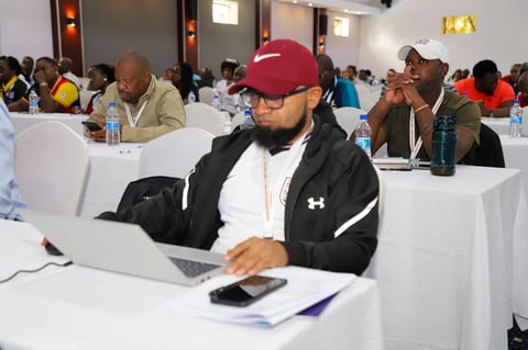 Man in red cap and black jacket working on laptop at conference table