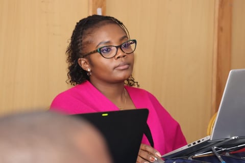 Woman wearing glasses and bright pink cardigan working at desk with laptop and tablet