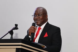 Man in black suit and red tie speaking at podium with microphone