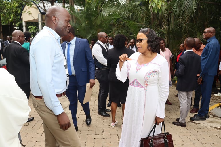 Man in light blue shirt and woman in white dress conversing at outdoor garden event with guests in background