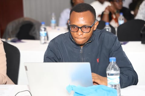 Man wearing glasses and navy jacket working on laptop at conference table