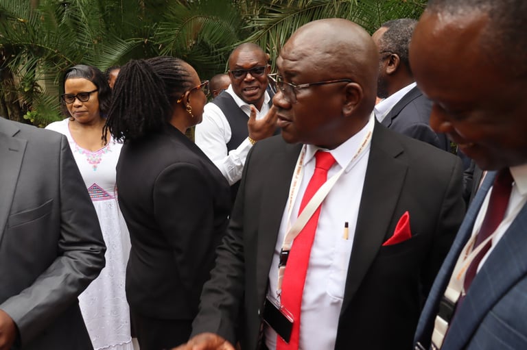 Group of formally dressed professionals gathered outdoors near palm trees, with a man in a red tie and black suit in the center